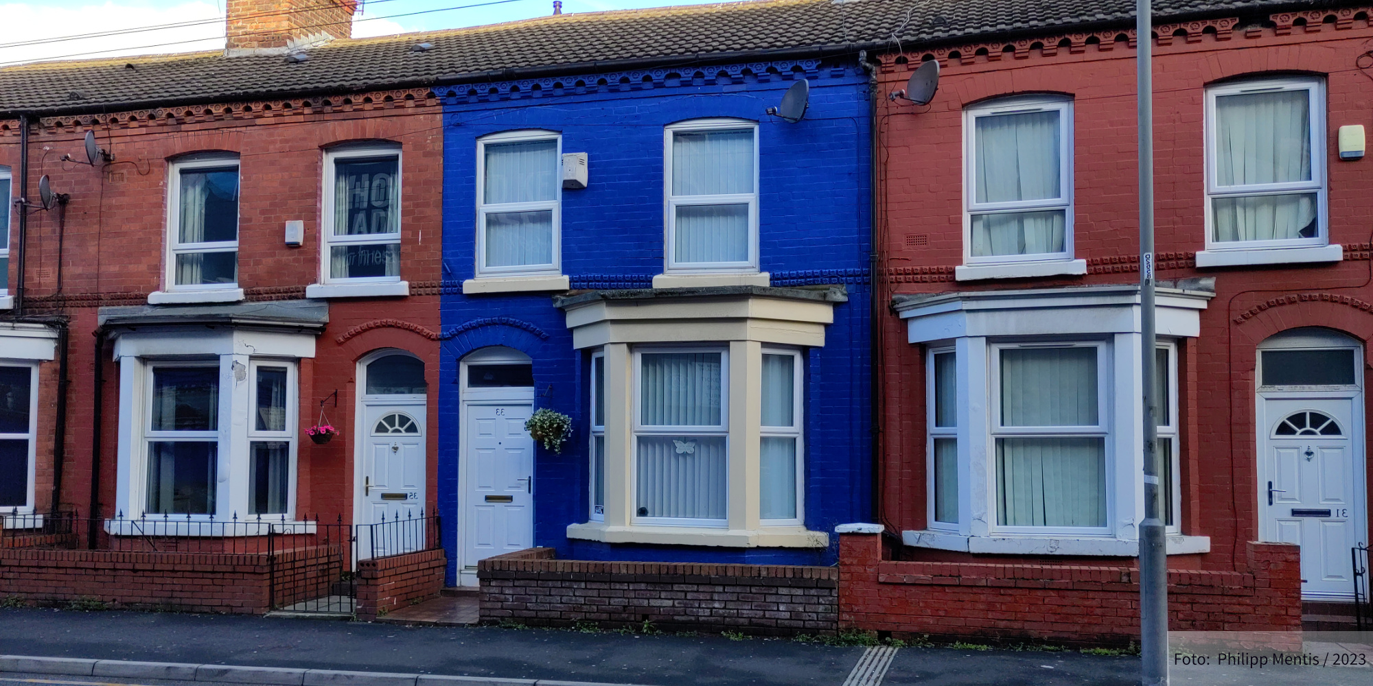 !B Three Houses lining a street in Liverpool. The one in the middle is painted in the colors of Everton, the other two are in LFC colors.