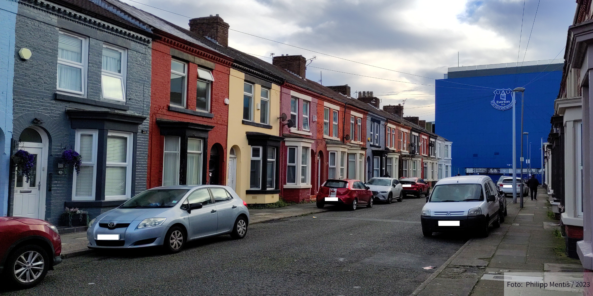 !B At the end of a street lined with colorfully painted houses stands Goodison Park - the home of Everton FC.