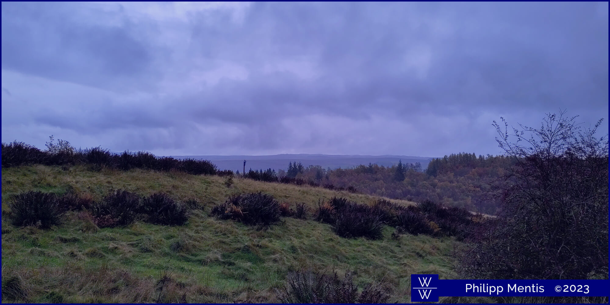 !B Grassy slopes of Loch Lomond National Park under a cloudy sky.